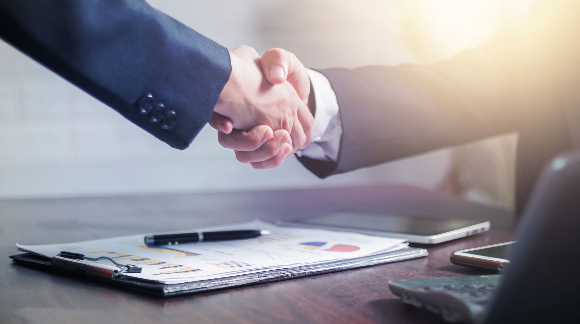 Professional handshake agreement over business charts in an office setting. — Why Businesses Are Choosing Nextcloud Hosting i